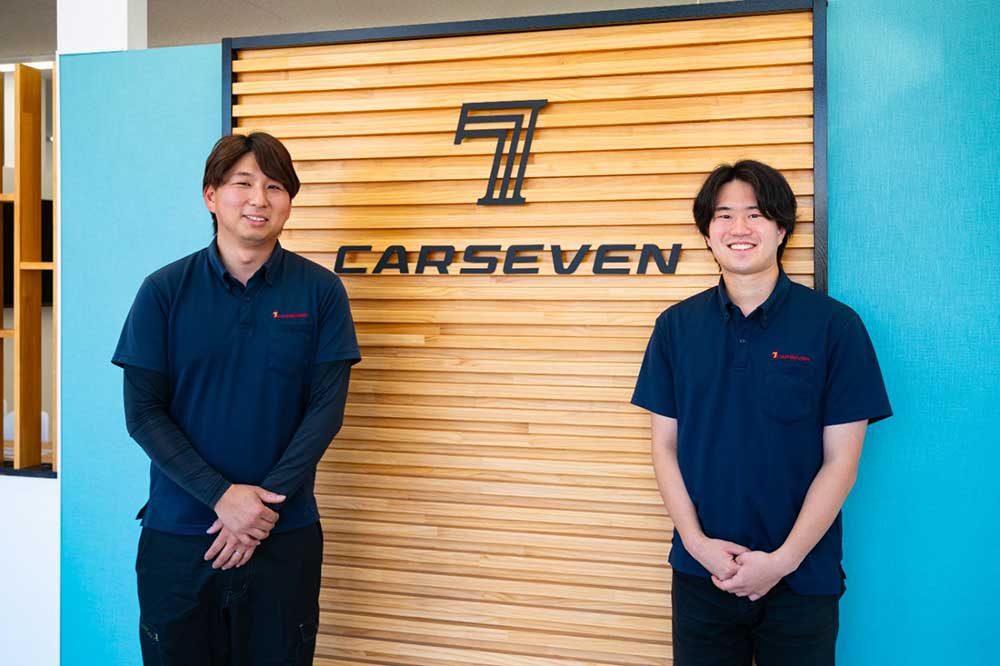 店舗ロゴの前に立つ新佐枝さん(左)と下山さん